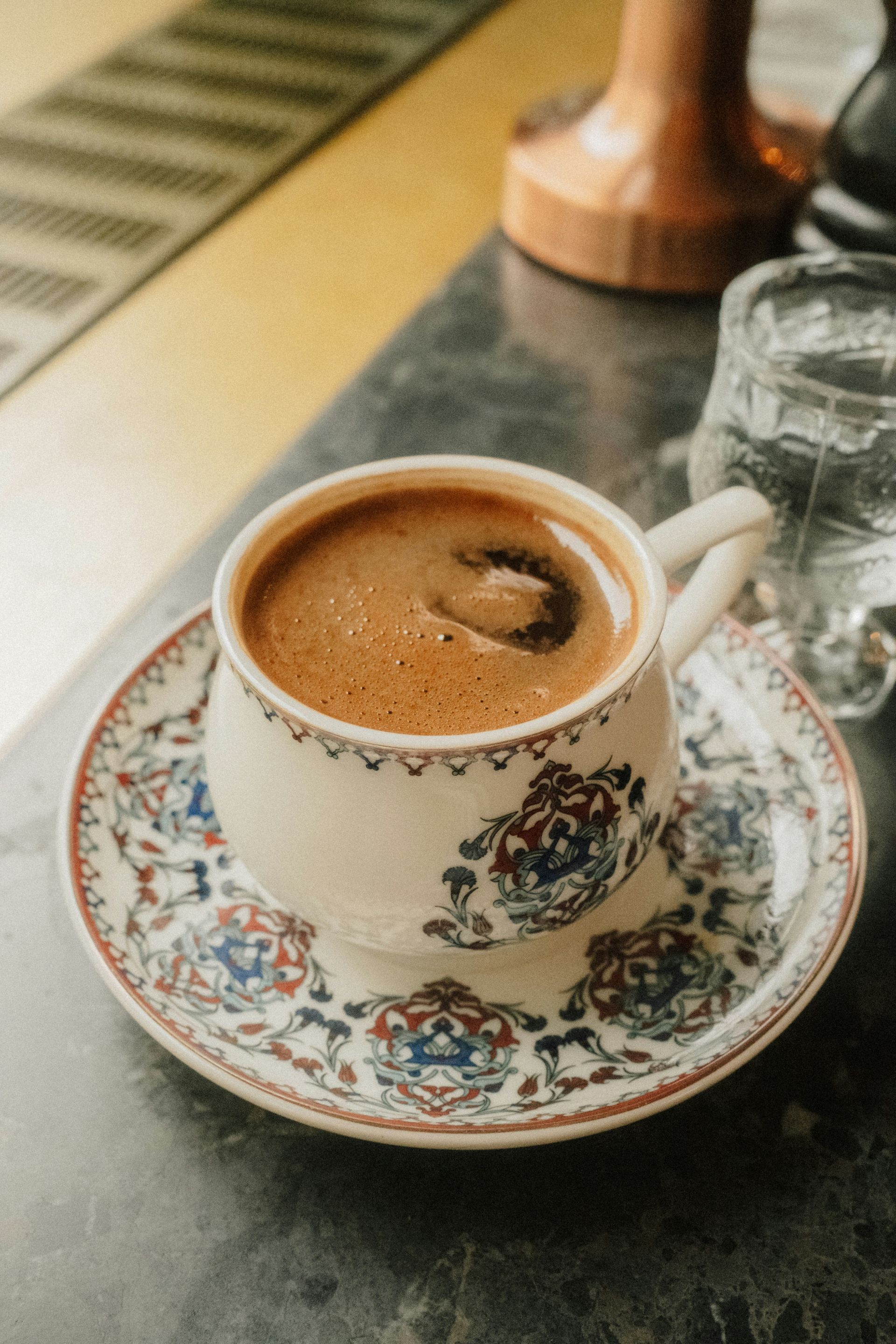A cup of dark coffee on a patterned saucer on a marble table