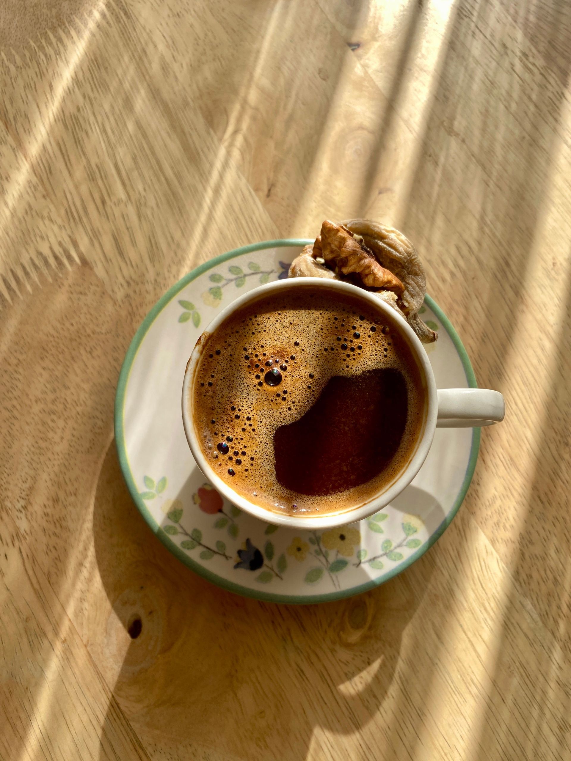 A steaming cup of coffee paired with a dried fig, captured on a sunlit wooden table.