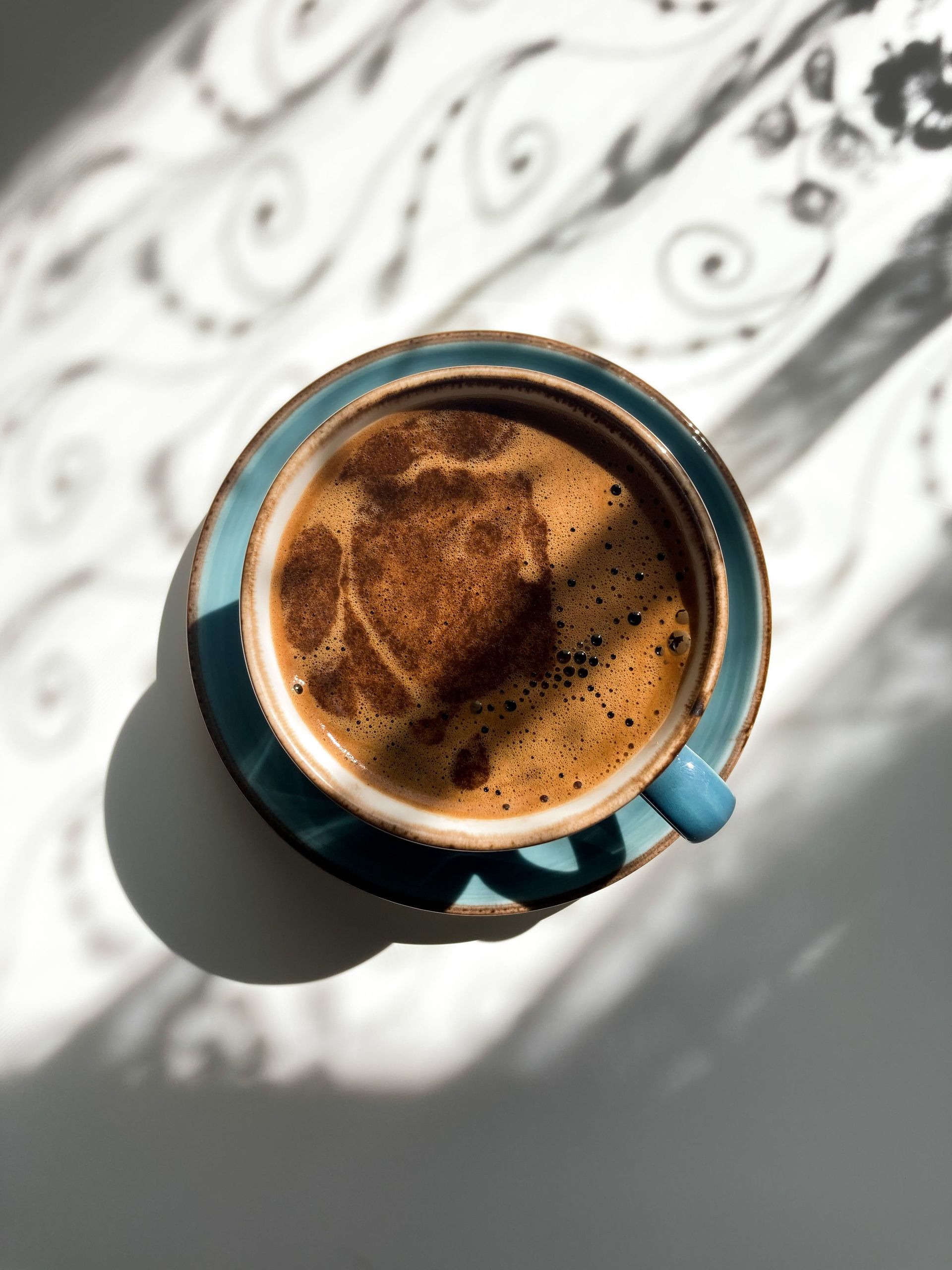 Coffee cup casting artistic shadows, viewed from above with swirling patterns. Perfect for caffeine and morning vibes.