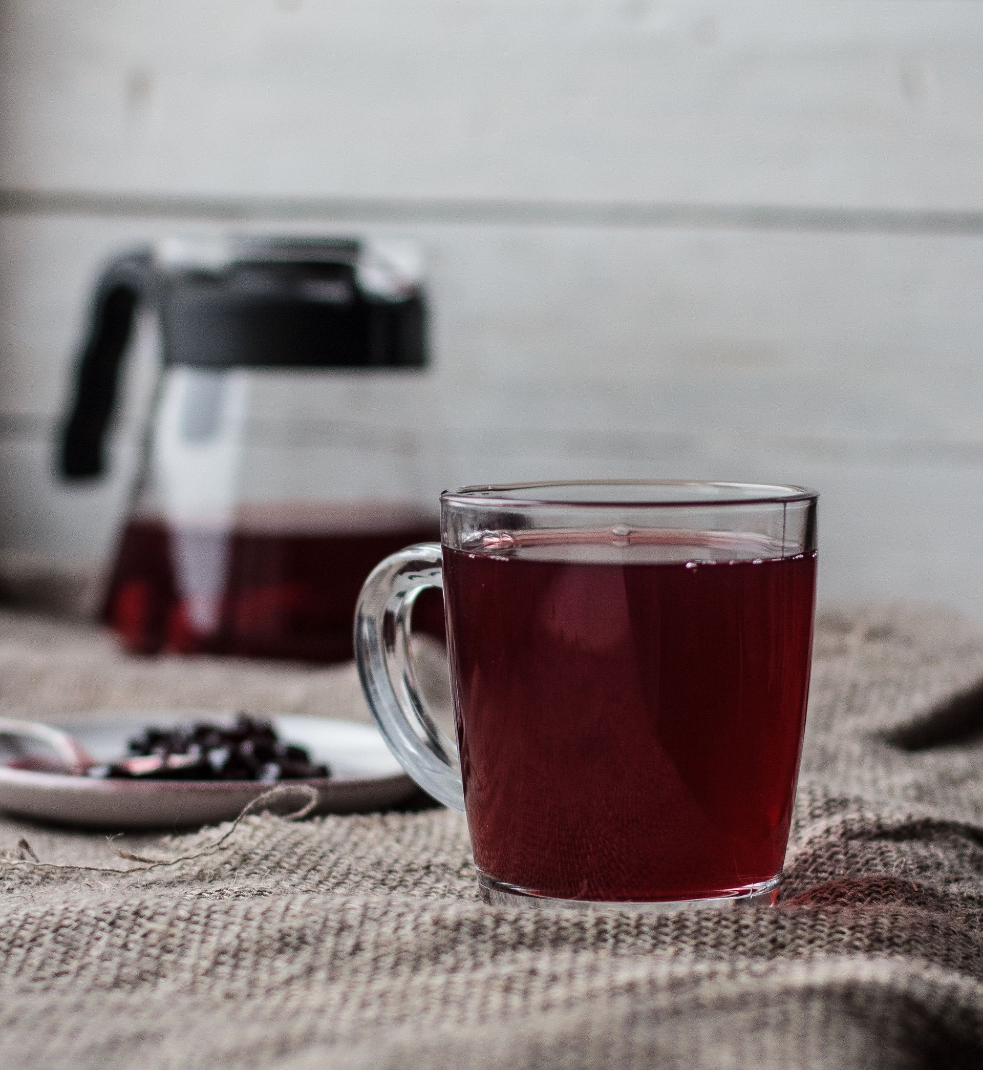 Glass cup with fragrant black tea and teapot placed on table covered with fabric tablecloth
